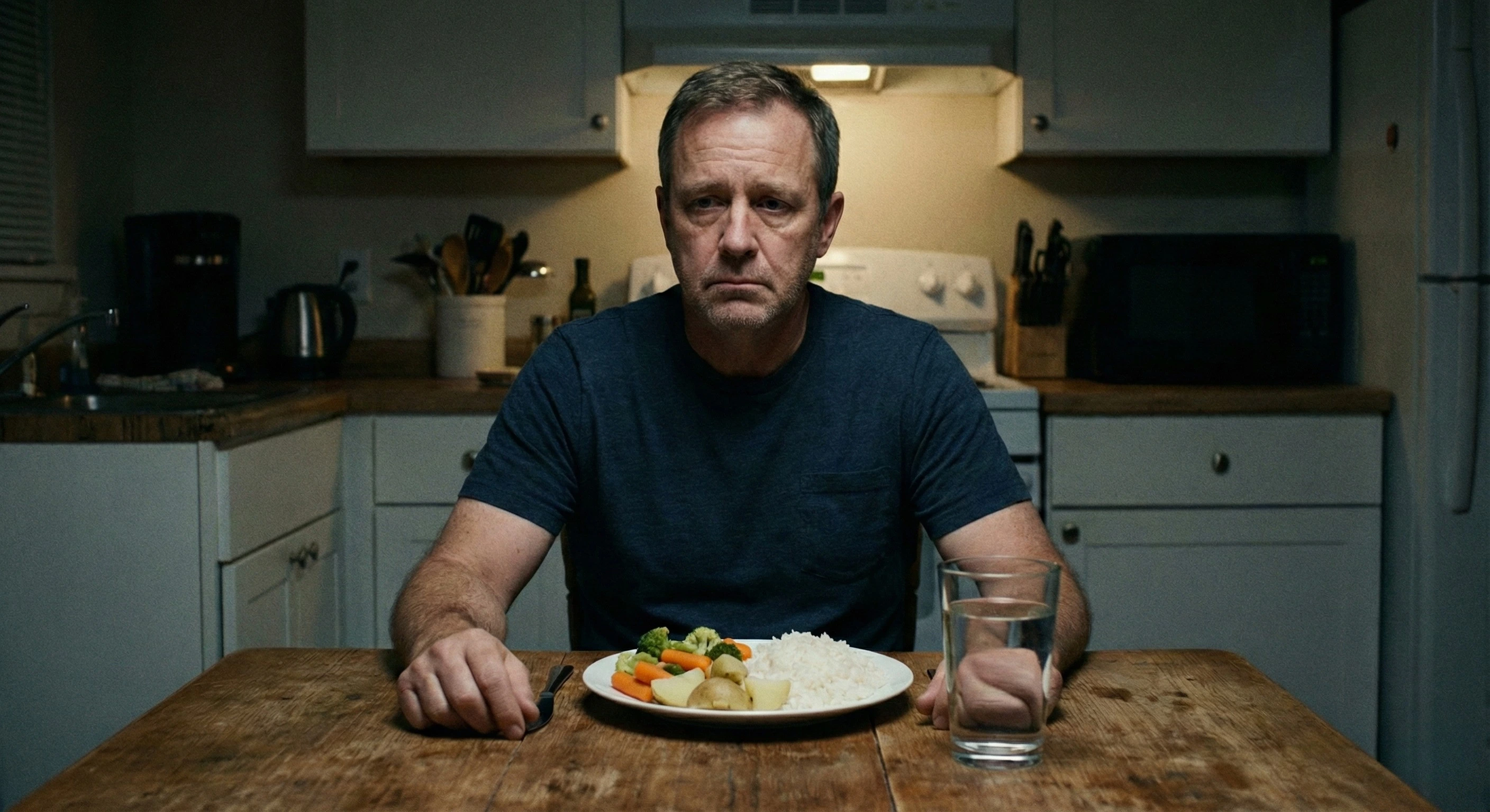 Uomo seduto a tavola con espressione triste mentre guarda un piatto di riso in bianco e verdure bollite, simbolo delle privazioni alimentari dovute alla gastrite